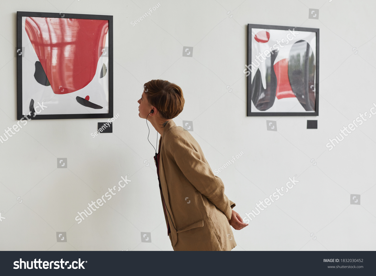 Wide angle portrait of tattooed young woman looking at paintings and listening to audio guide at modern art gallery exhibition, copy space #1832030452