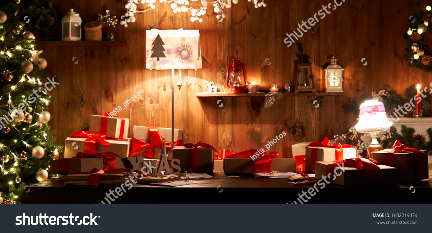 Decorated xmas table with Merry Christmas gifts in cozy Santa home interior, banner. Happy New Year presents boxes in workshop late in night with lights on xmas tree, holiday eve background. #1832219479