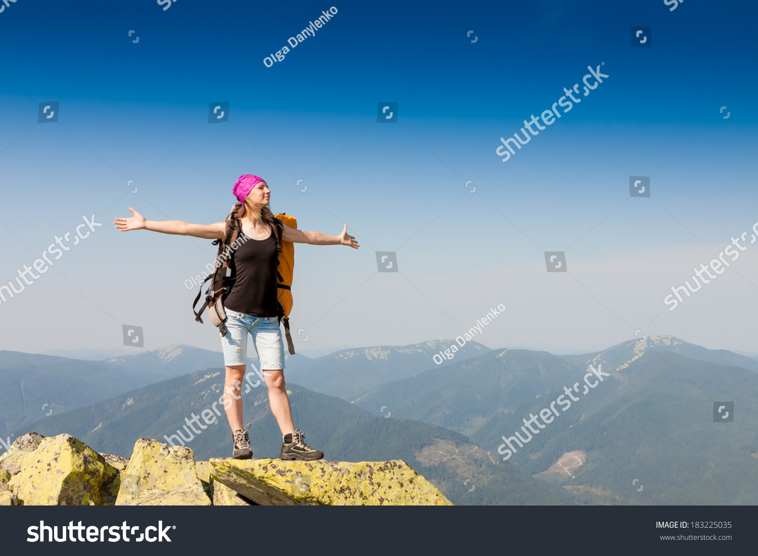 Hiker with backpack standing on top of a mountain and enjoying the view  #183225035