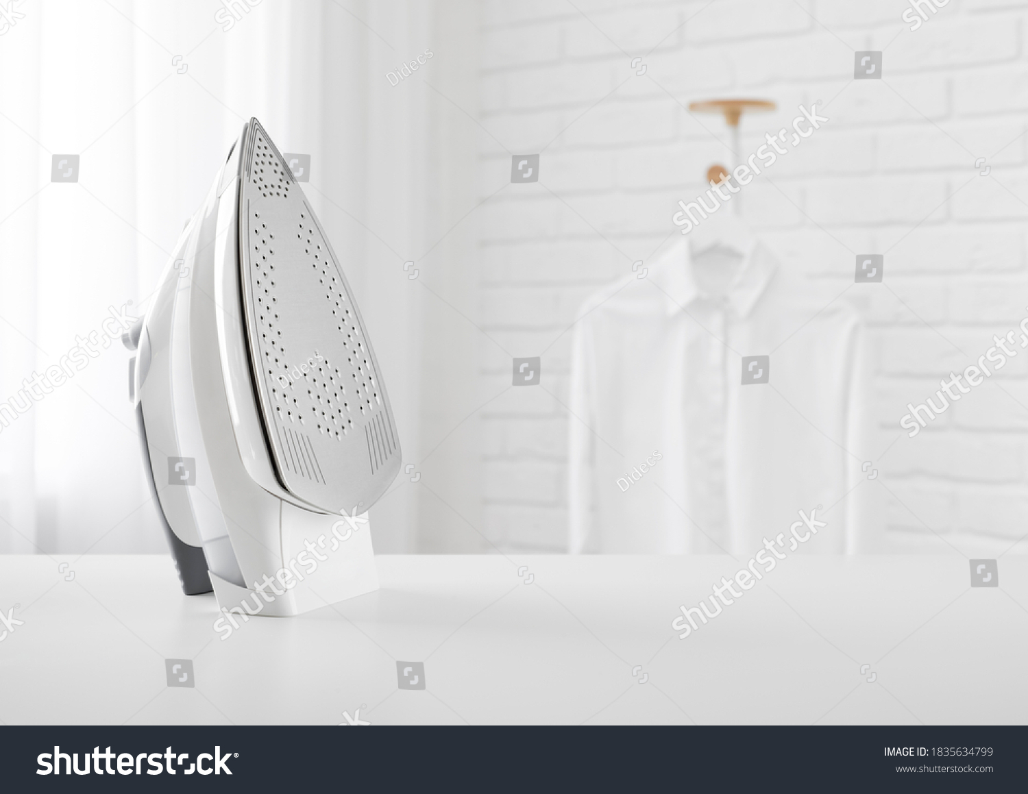 Electric iron on table in blurred room with clothes rack #1835634799