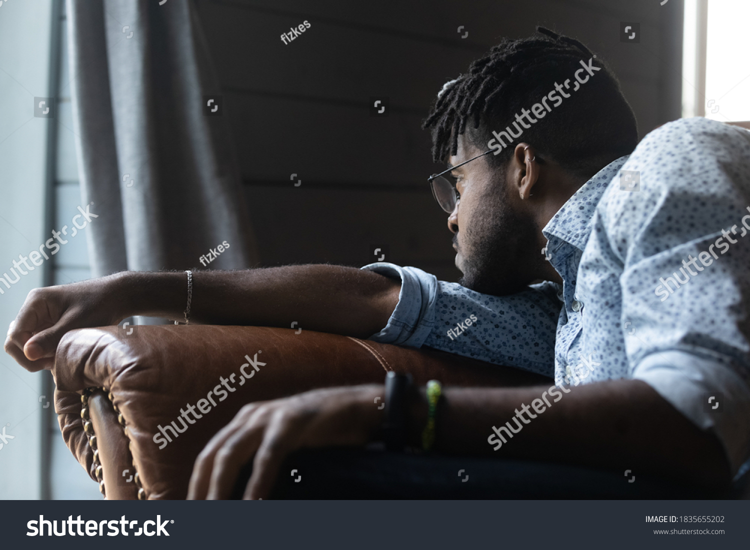 Upset young African American male sit on sofa at home look in distance mourning missing. Unhappy sad biracial guy distressed with life problems, feel lonely thinking or pondering. Solitude concept. #1835655202