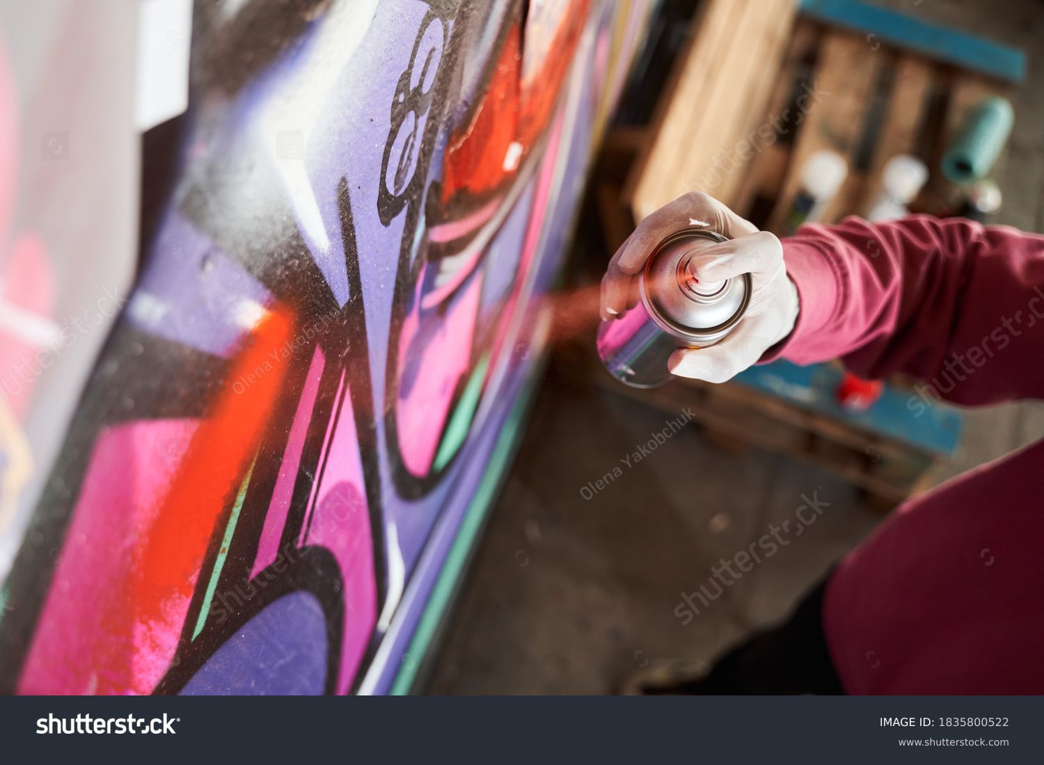 Detail of street artist painting colorful graffiti on public wall. Modern art concept with urban guy drawing live murales with multi color aerosol spray. Focus on the boy hand with spray paint can #1835800522