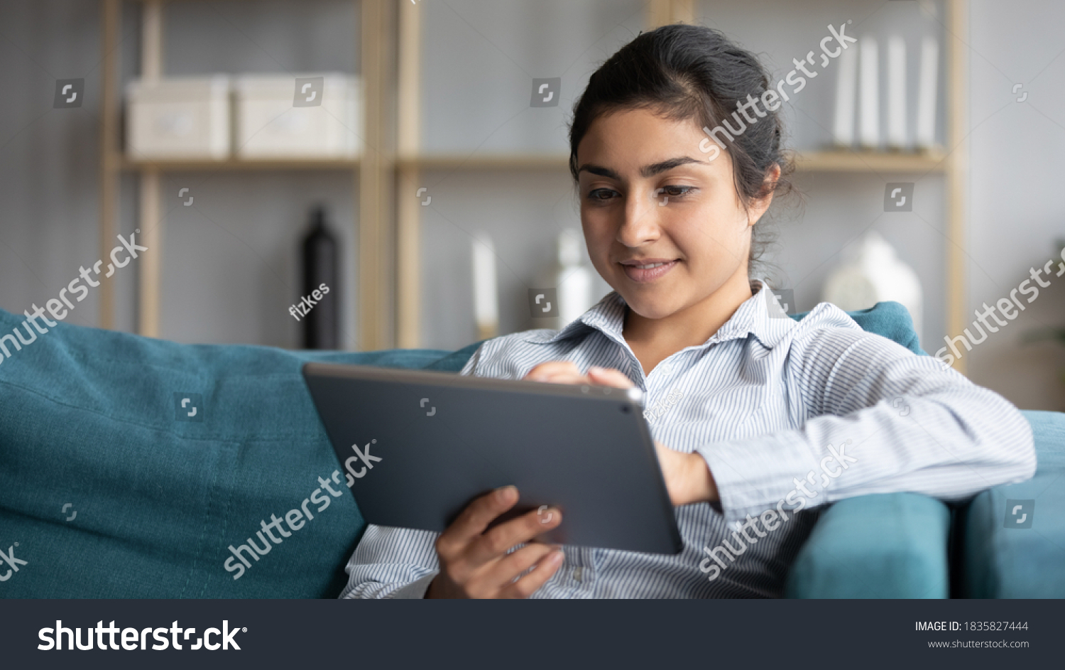 Calm indian woman resting on couch at home hold tablet modern device smile read message enjoy remote shopping online, distance chat with friend, plan vacation booking hotel and travel buy tour concept #1835827444
