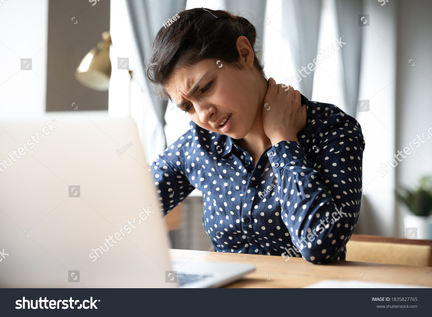 Pinched nerves, tensed sore muscles, fibromyalgia ache due sedentary lifestyle and incorrect posture concept. Indian ethnicity frowning woman sitting at desk in front of laptop, touch neck feels pain #1835827765