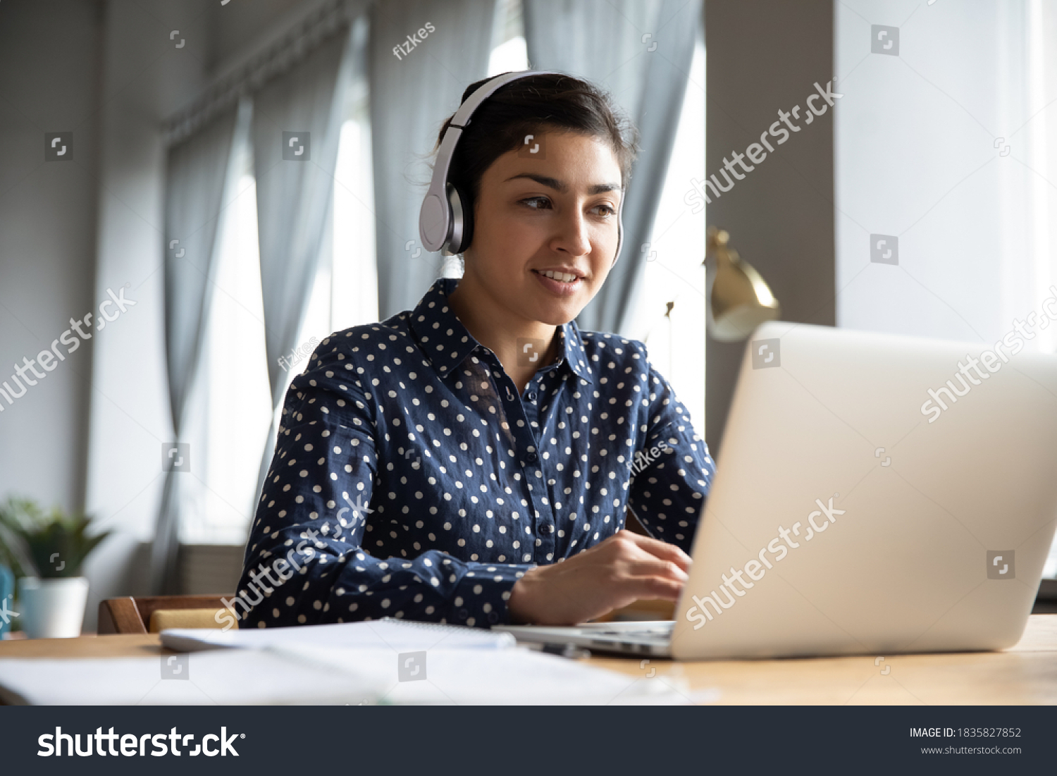 Indian business woman sit at desk wearing headphones lead negotiations through videoconference call with clients consulting customer use laptop. Educational webinar, on-line class distantly concept #1835827852