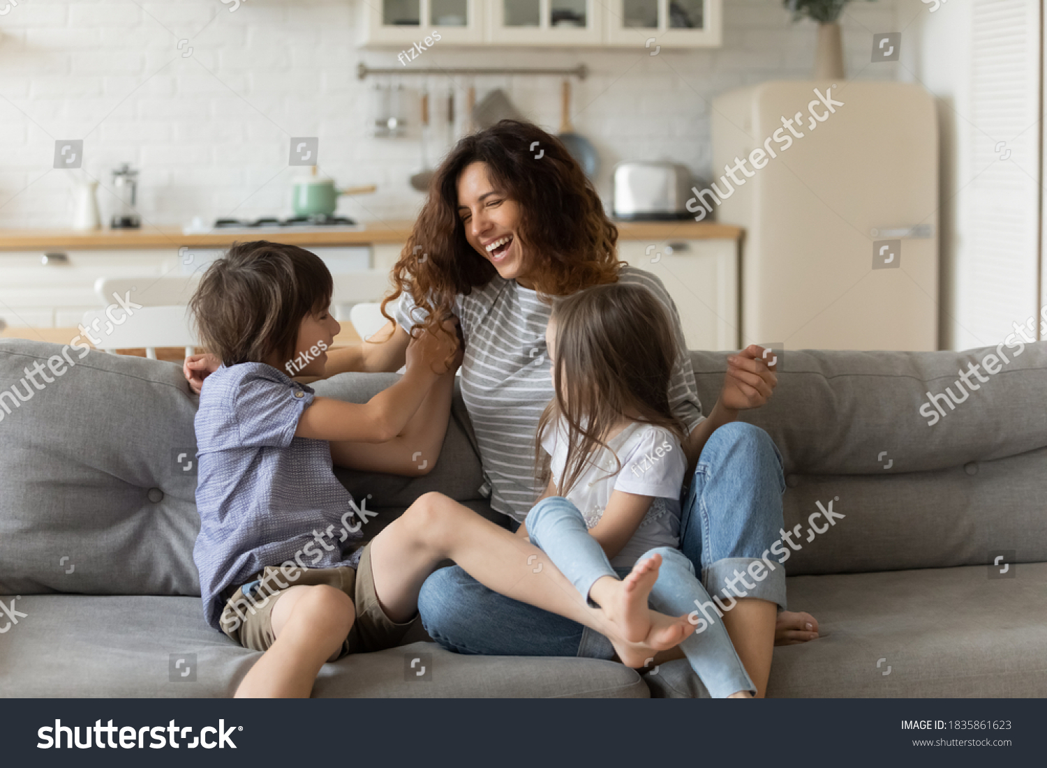 Overjoyed young mother having fun with two kids at home, laughing happy mum, adorable little daughter and son playing funny active game, tickling, sitting on cozy couch in living room #1835861623