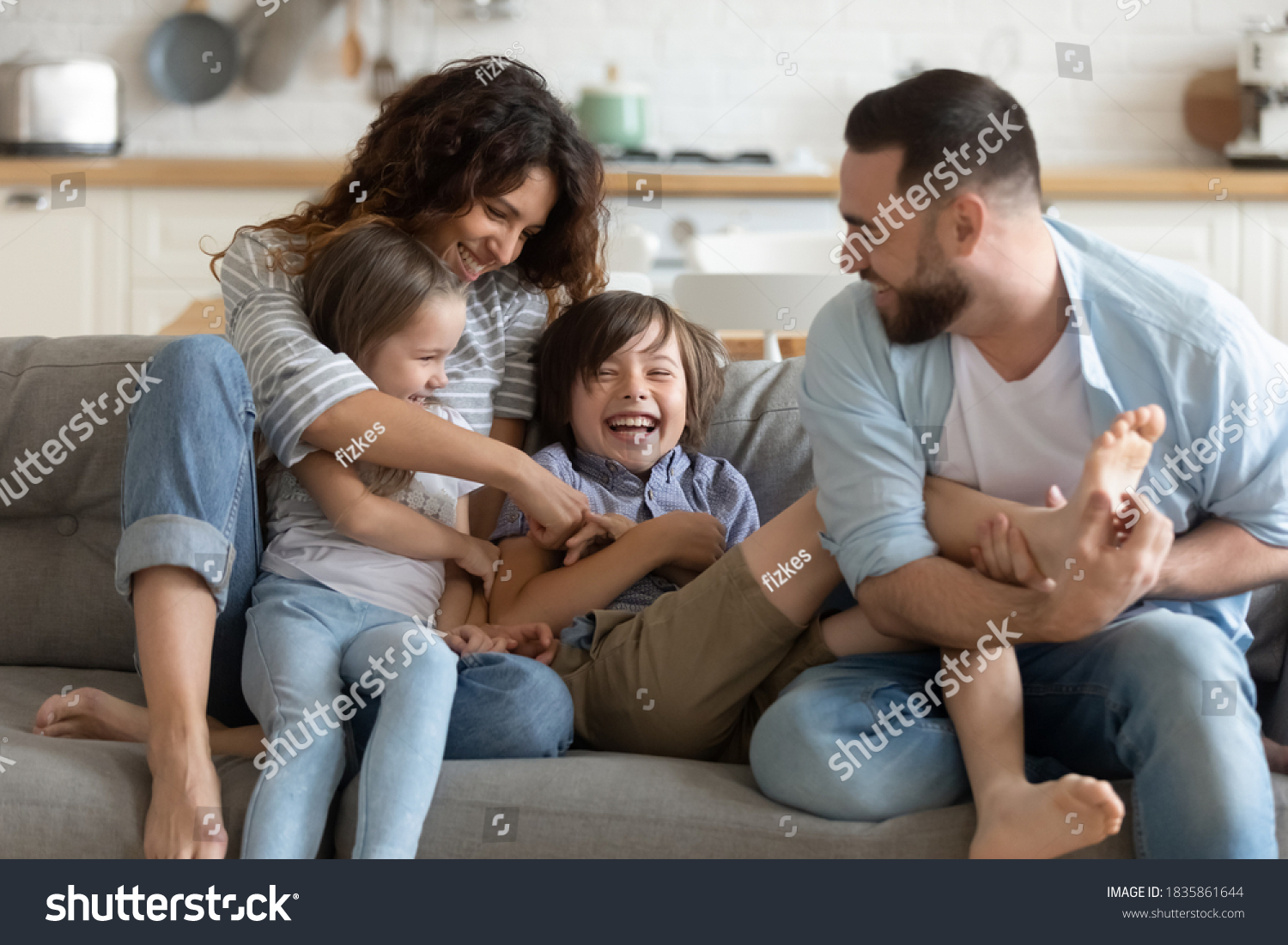 Happy young parents with two kids having fun at home, laughing overjoyed mother and father tickling little daughter and son, sitting on couch in living room, family enjoying leisure time together #1835861644