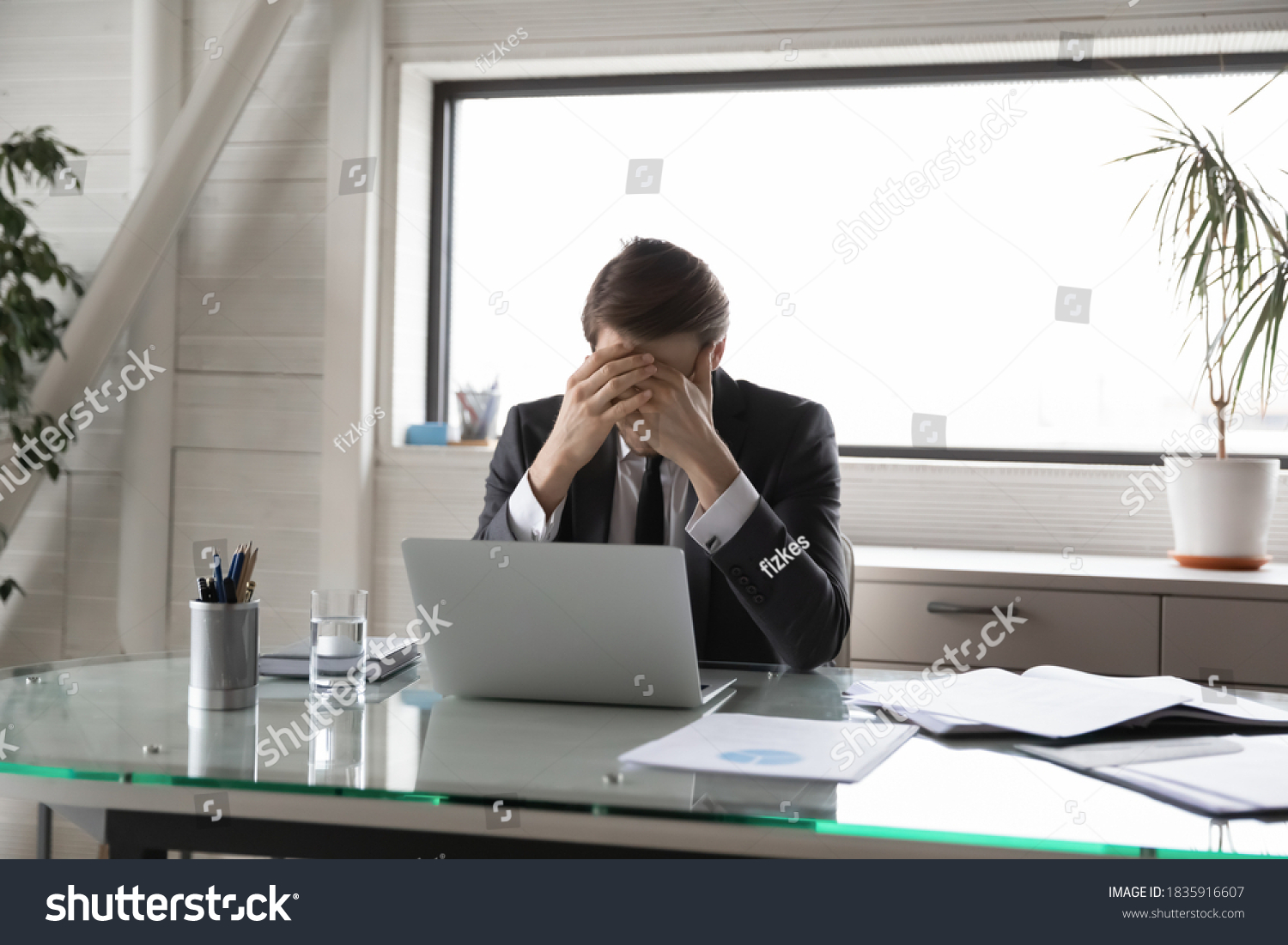 Unhappy young male manager covering head with hands, suffering from pressure at work or feeling unwell due to overload. Overworked stressed businessman workaholic having headache, needs rest. #1835916607