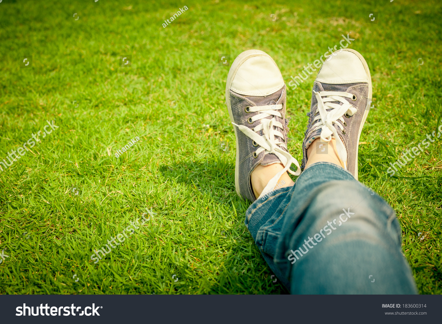 youth sneakers on girl legs on grass during sunny serene summer day. #183600314