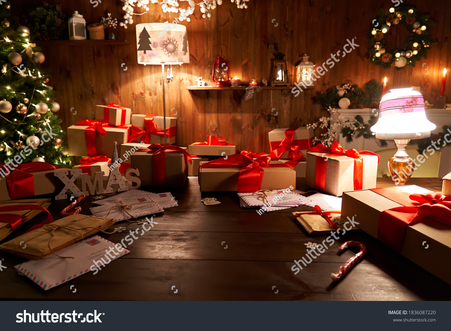 Santa Claus workshop home wooden decorated table with Merry Christmas tree, decor, wrapped gifts presents boxes on holiday eve in cozy home interior late in night with lamp light on xmas background. #1836087220