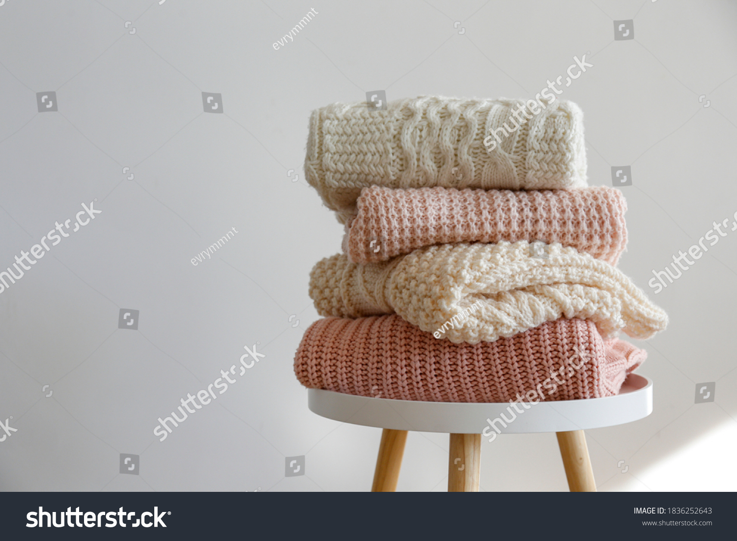 Stack of clean freshly laundered, neatly folded women's clothes on wooden table. Pile of shirts, dresses and sweaters on the table, white wall background. Copy space, close up, top view. #1836252643