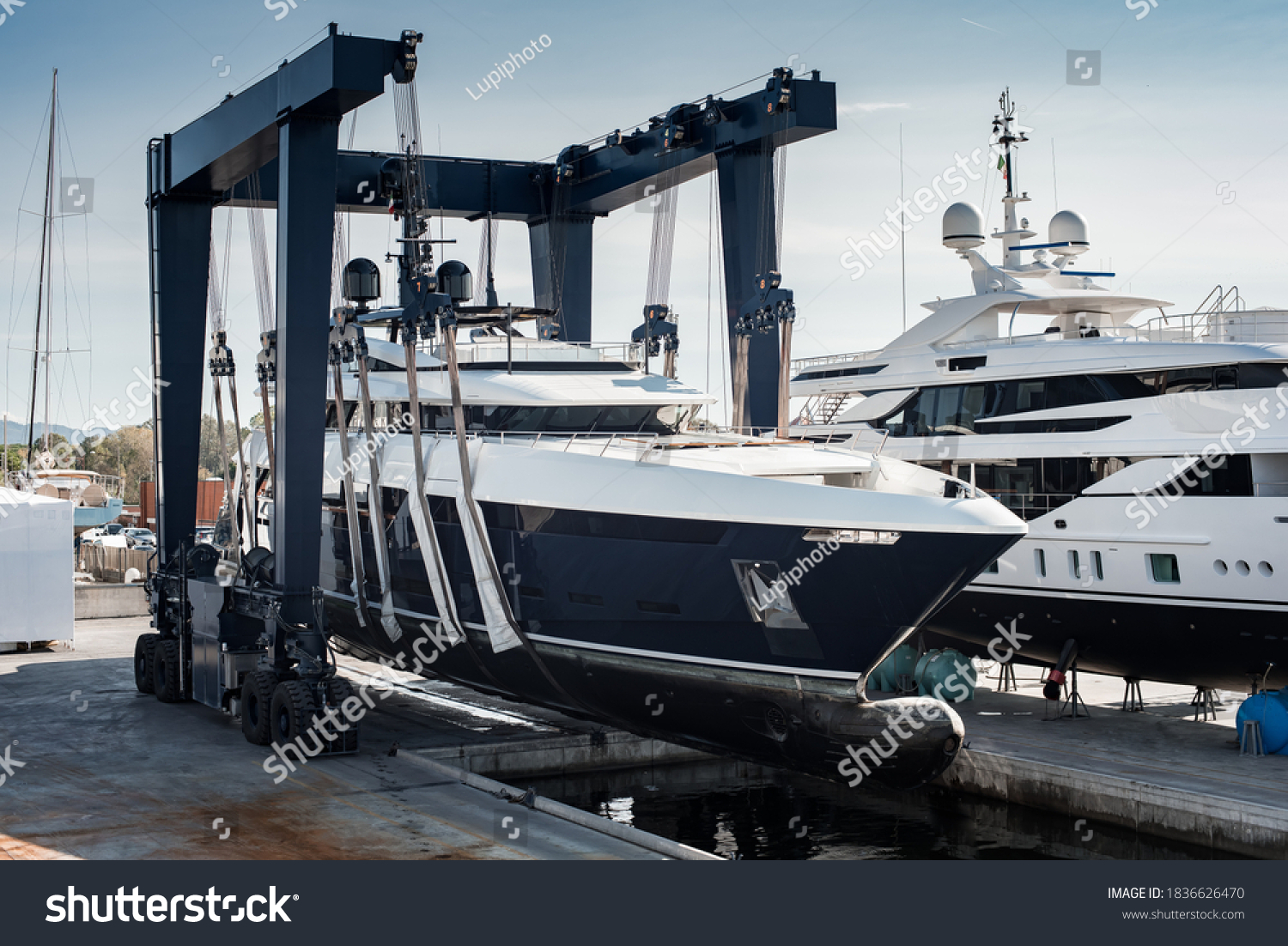 Super Yacht hauled out in shipyard, being lifted by industrial crane for refit or maintenance yard period  #1836626470