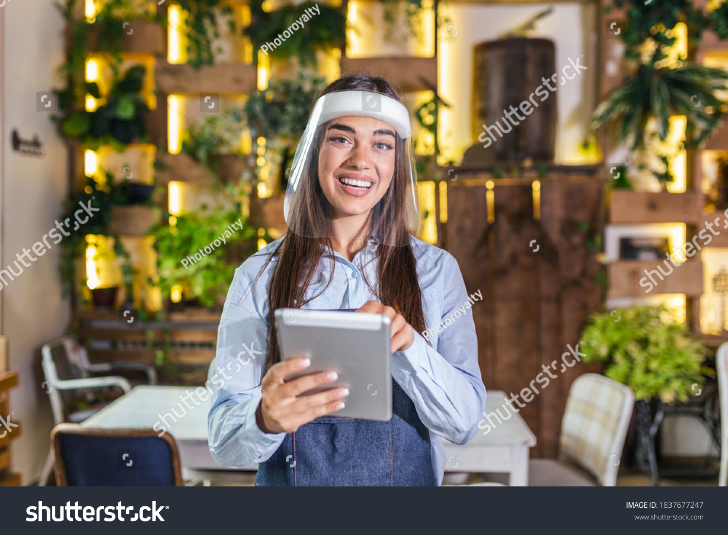 Happy female waitress using digital tablet while wearing visor at the restaurant or cafe. Open again after lock down due to outbreak of coronavirus covid-19, New normal #1837677247