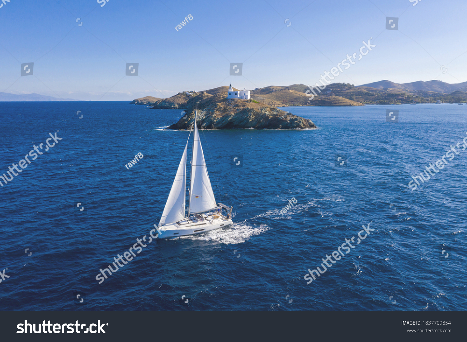 Sailing. Sailboat with white sails, rippled sea background, Lighthouse on a cape. Greece, Kea Tzia island. Summer holidays in Aegean sea. Aerial drone view #1837709854