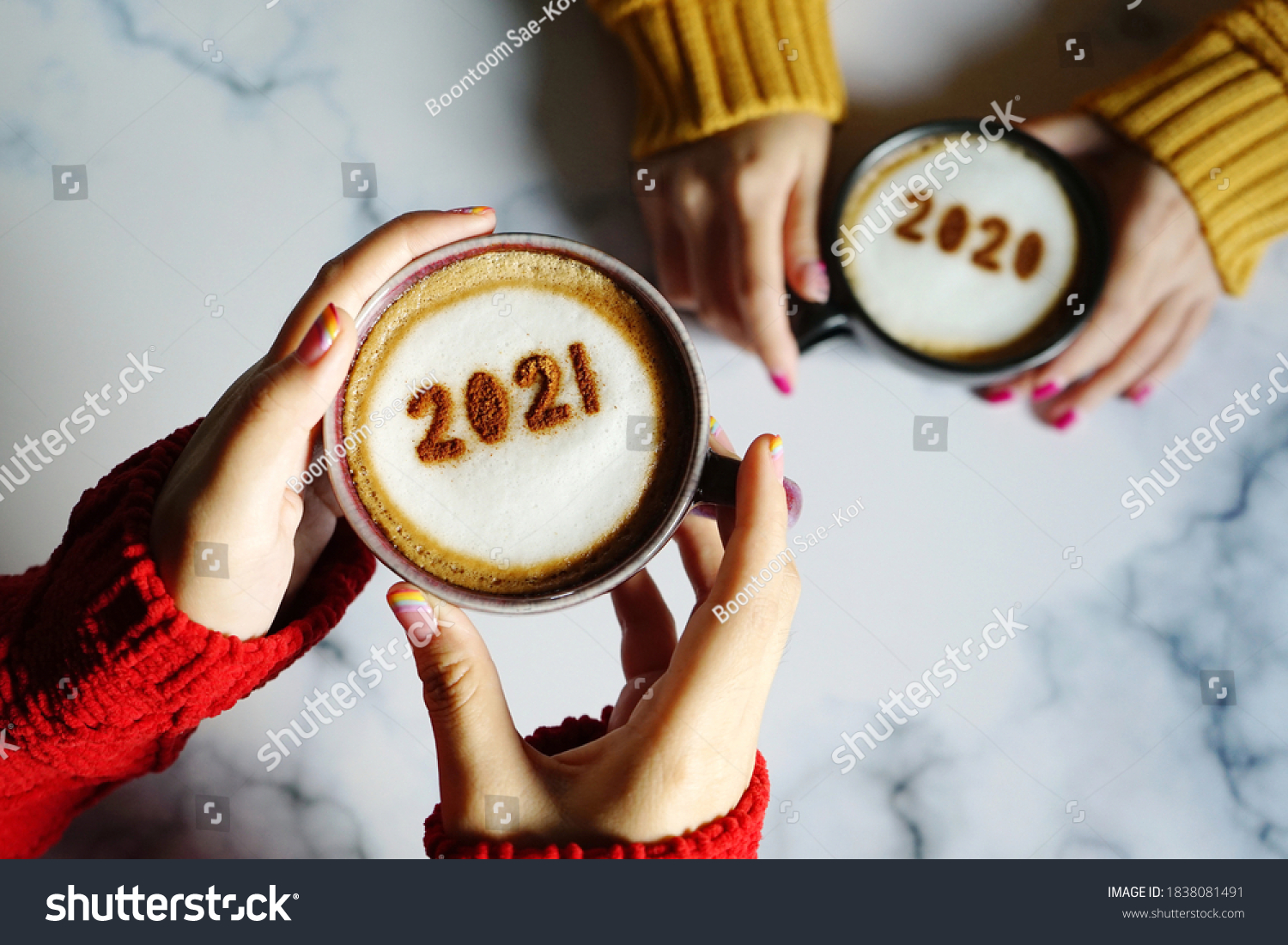 Goodbye 2020, Hello 2021 theme coffee cup with number 2021 on frothy surface in female hands holding and another one with number 2020 on frothy surface over marble table background. Holidays food art. #1838081491