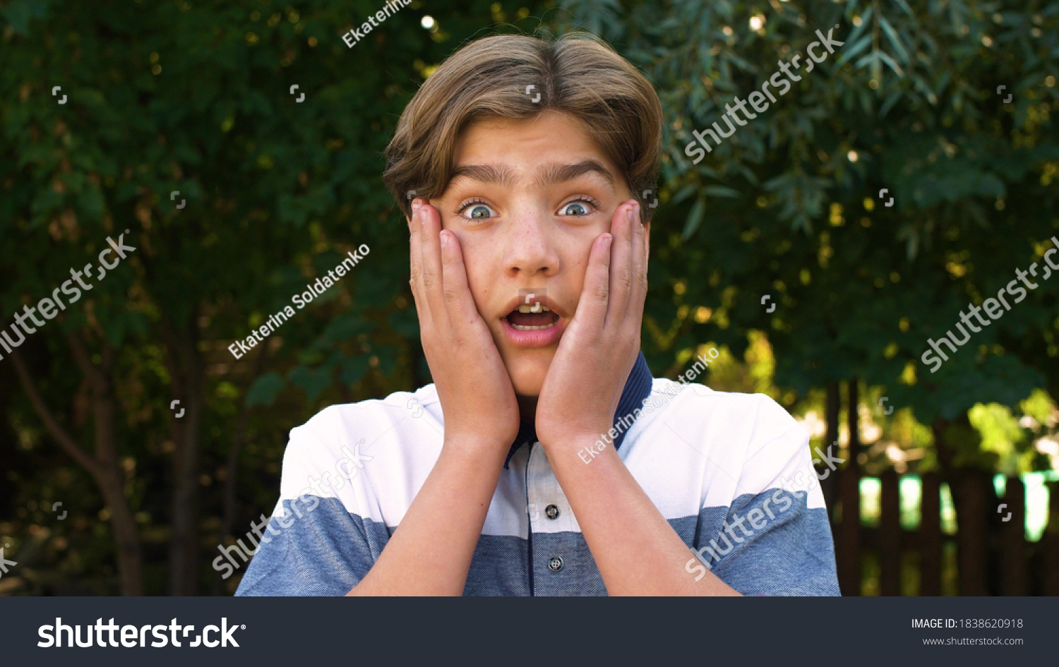 Close-up of the face of a young, cute, Caucasian boy who is surprised and puts the palms of his hands to his cheeks. Positive emotion. On the street. #1838620918