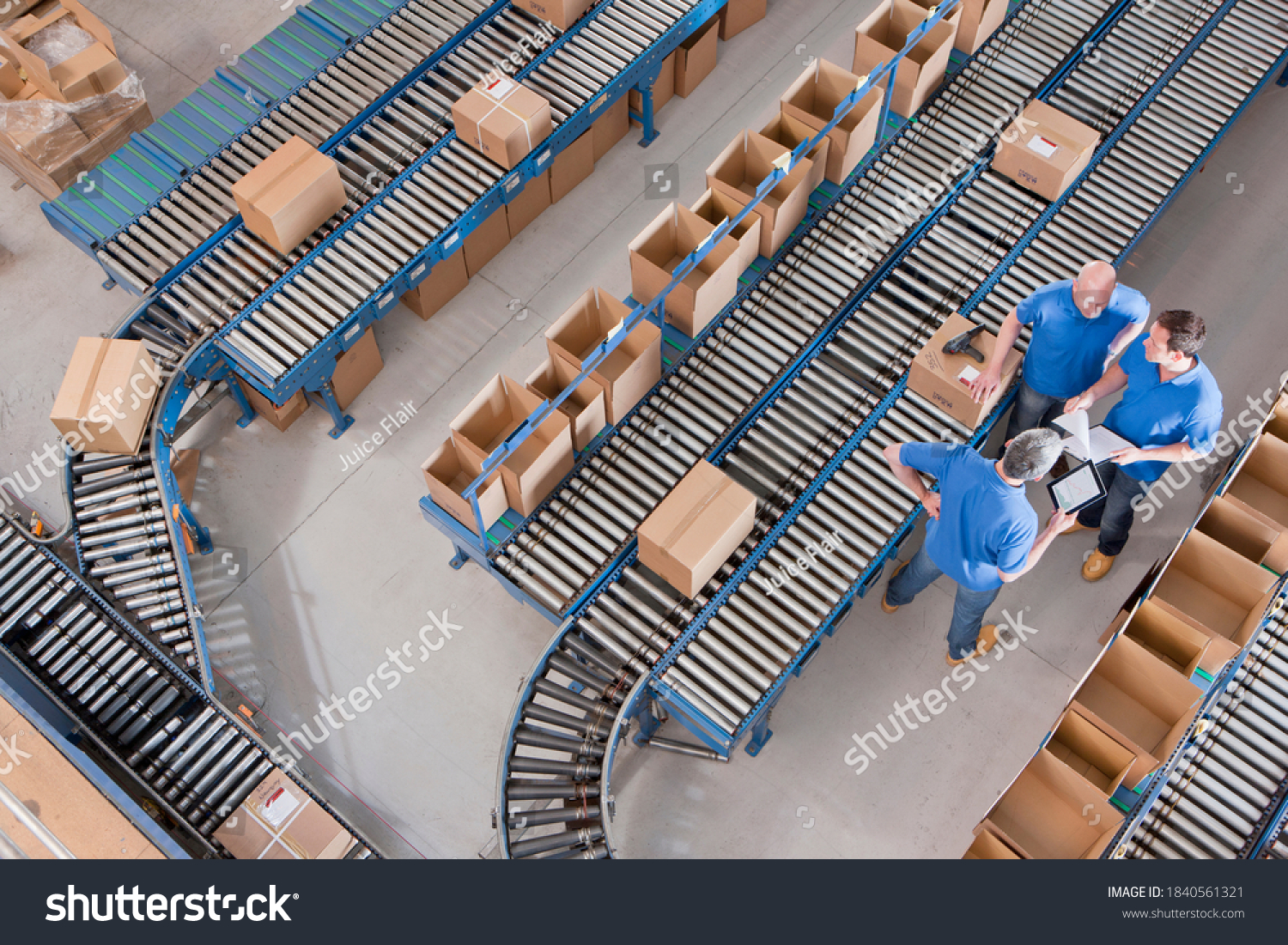 Top view of workers with papers and a digital tablet having a discussion among boxes laid on conveyor belts at a distribution warehouse. #1840561321
