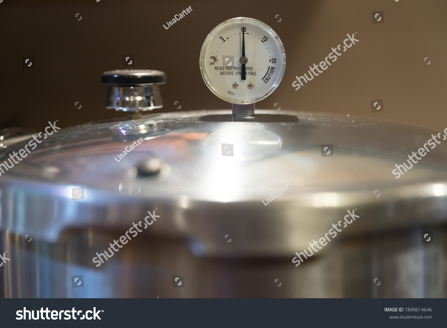 A stainless steel pressure cooker lid with pressure gauge reading 10 pounds of pressure. Pressure canners are used to can vegetables from the garden. #1840614646
