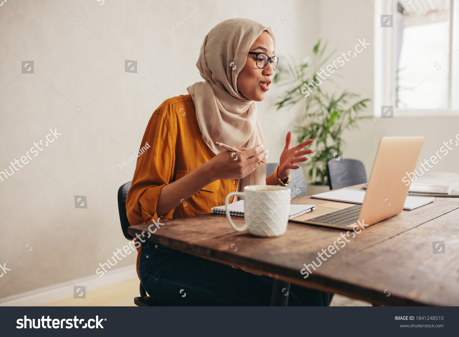 Muslim businesswoman working at home due to pandemic isolation. Female wearing hijab talking over a video call with team. #1841248510