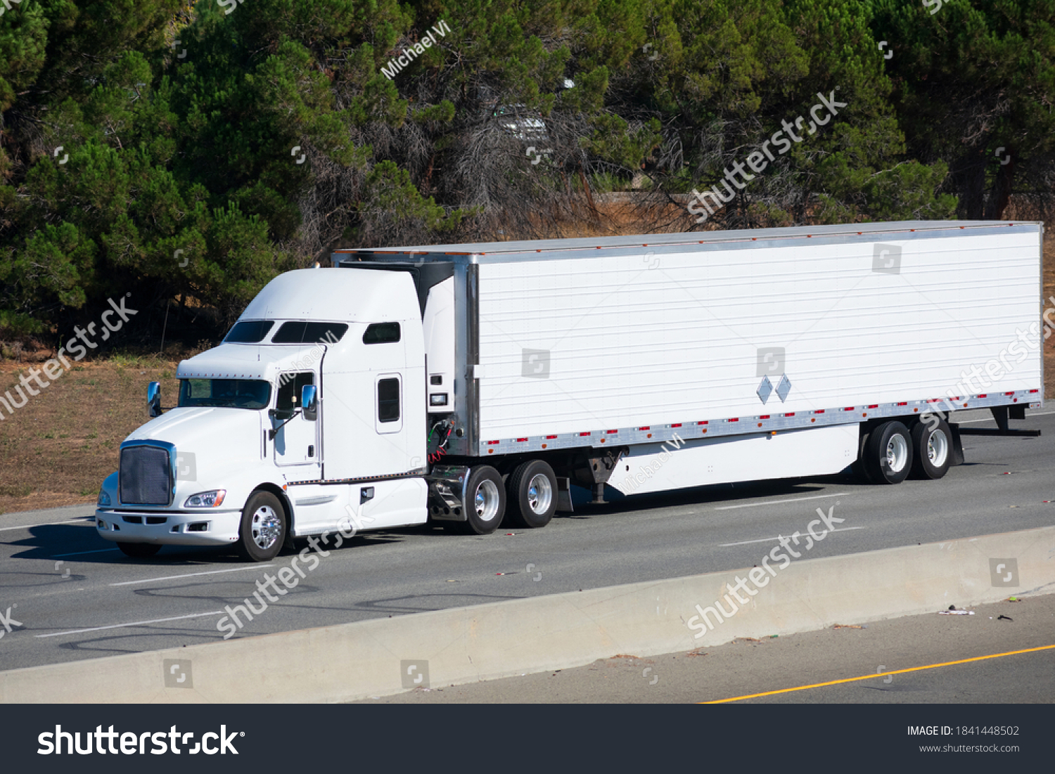 White big rig long haul semi truck transporting commercial cargo in refrigerator semi truck running alone on the eight lanes highway #1841448502