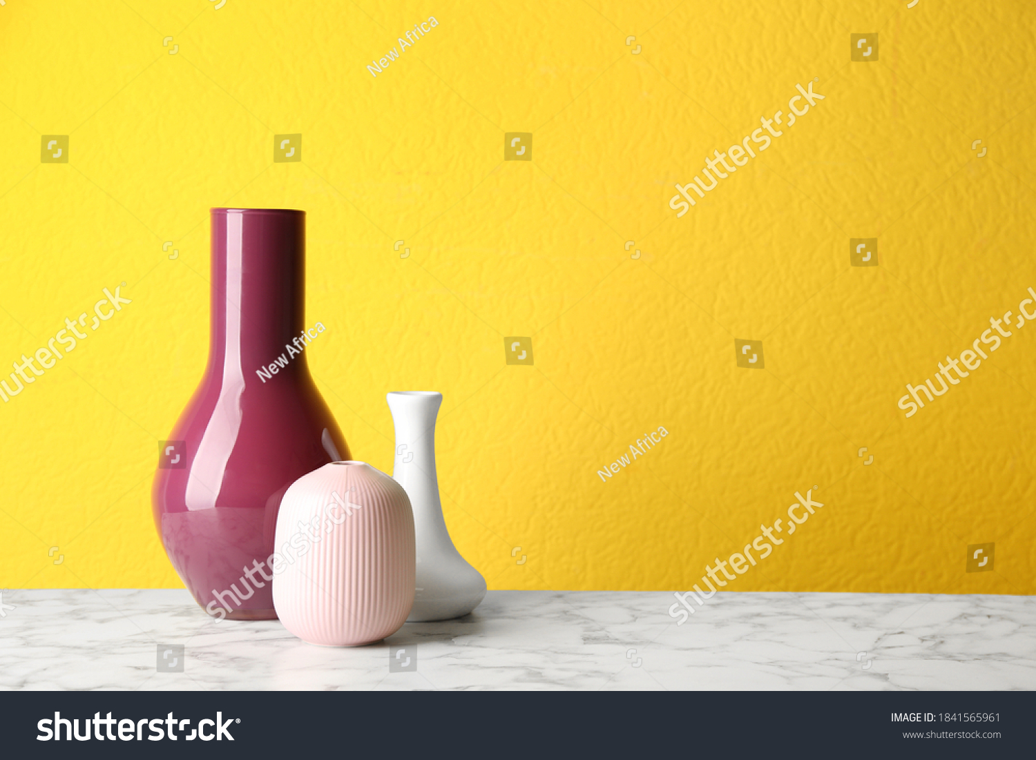 Stylish ceramic vases on white marble table against yellow background. Space for text #1841565961