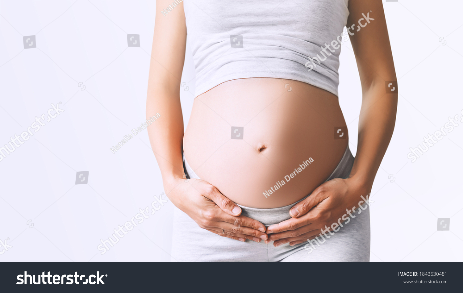 Pregnant woman holds hands on her belly on white background, close-up. Beautiful photo of pregnancy. Mother waiting for baby. Women prepare for maternity. Concept of prenatal period, maternal health. #1843530481