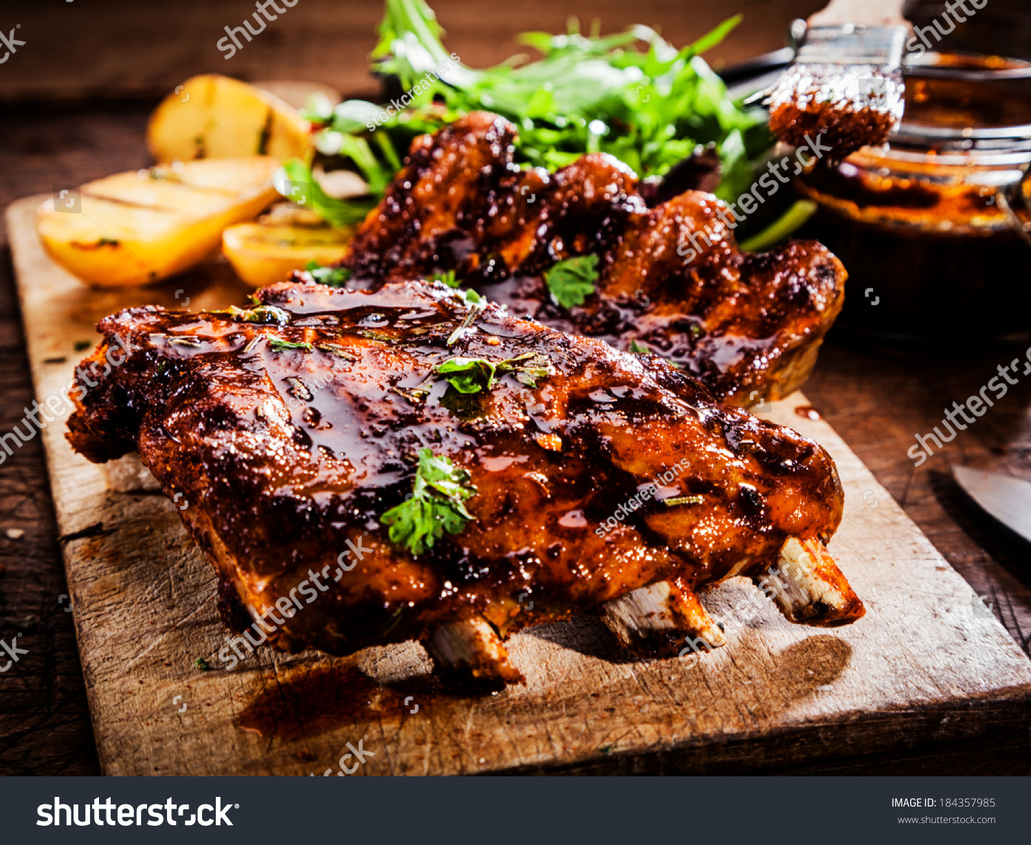 Delicious barbecued ribs seasoned with a spicy basting sauce and served with chopped fresh herbs on an old rustic wooden chopping board in a country kitchen #184357985