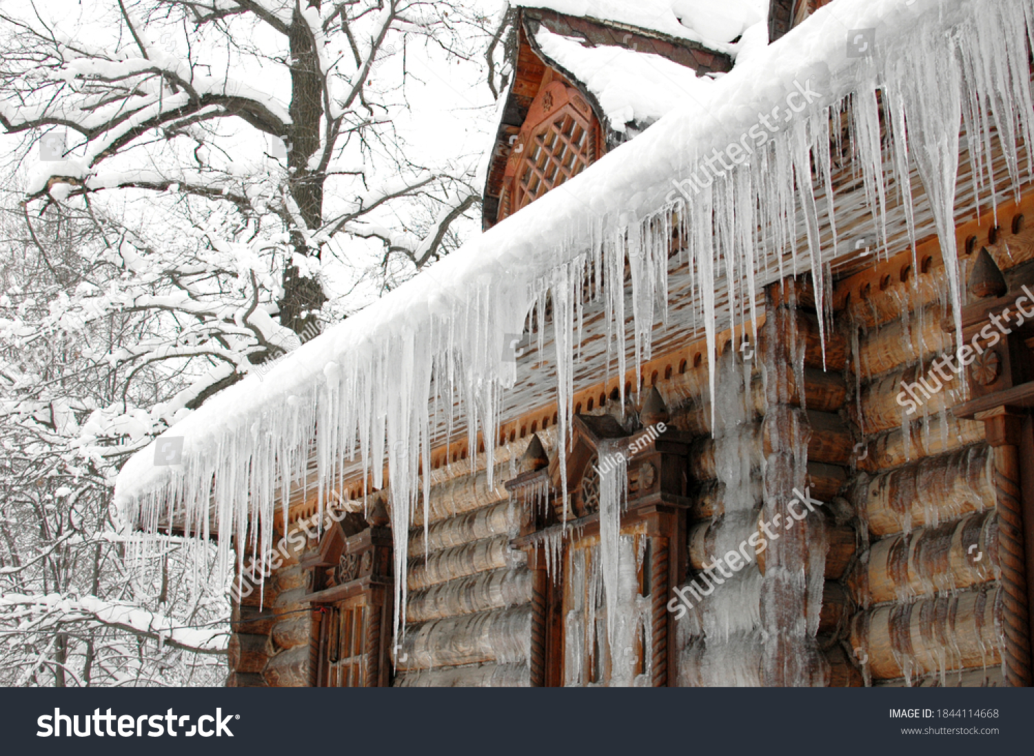 Icicles in winter. The old hut is covered with ice in winter. Icicles hang from the roof. The wooden tower is covered with ice. Icicles hang on the roof of a house. The logs of the hut were frozen #1844114668