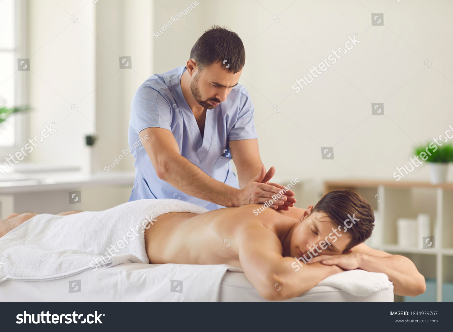Relieving back muscle tension. Professional masseur massaging young man's back using Tapotement or chopping, tapping or hacking technique during Swedish massage therapy in spa salon or wellness center #1844939767