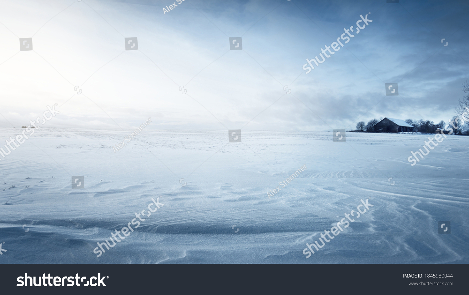 Panoramic view of the snow-covered field after a blizzard at sunset. Human tracks in a fresh snow. Old rustic wooden house in the background. Ice desert. Global warming theme. Lapland, Finland #1845980044