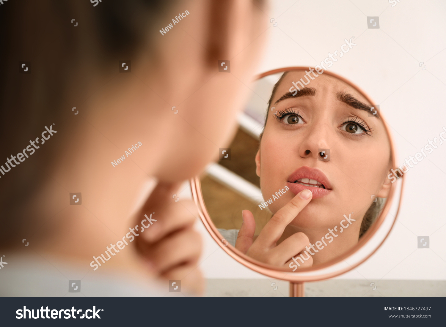 Emotional woman with herpes touching lips in front of mirror against light background #1846727497