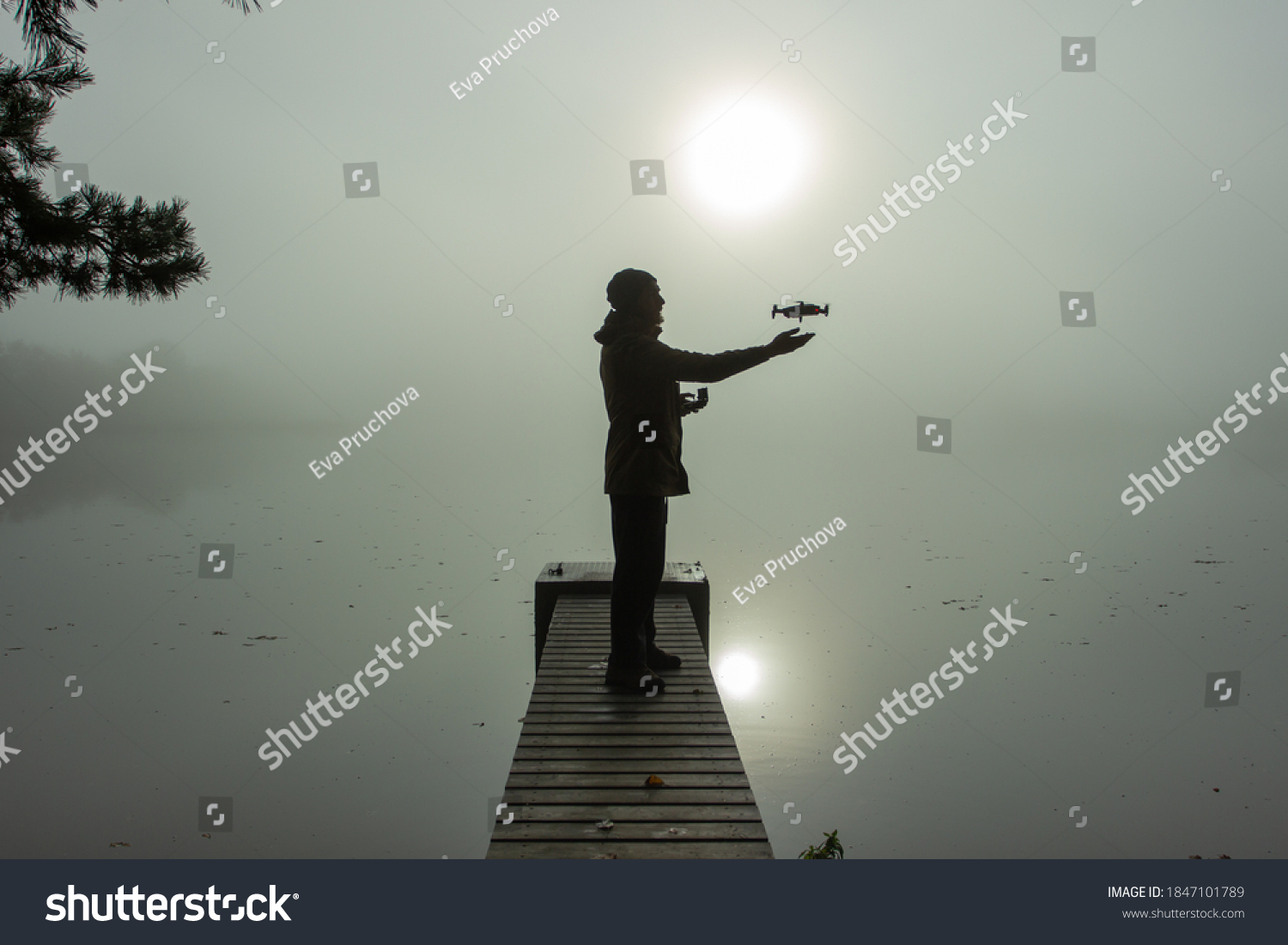 Man playing with the drone. Silhouette against the foggy landscape.Male operating the drone by remote control and having fun. Pilot flying drone. Use of drone outdoors, piloting and media work #1847101789