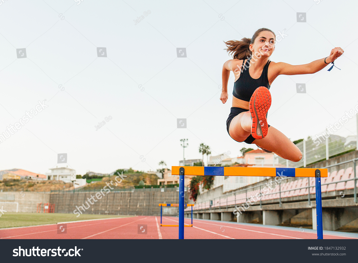 Fit female teenager athlete hurdler running jumping over hurdles #1847132932