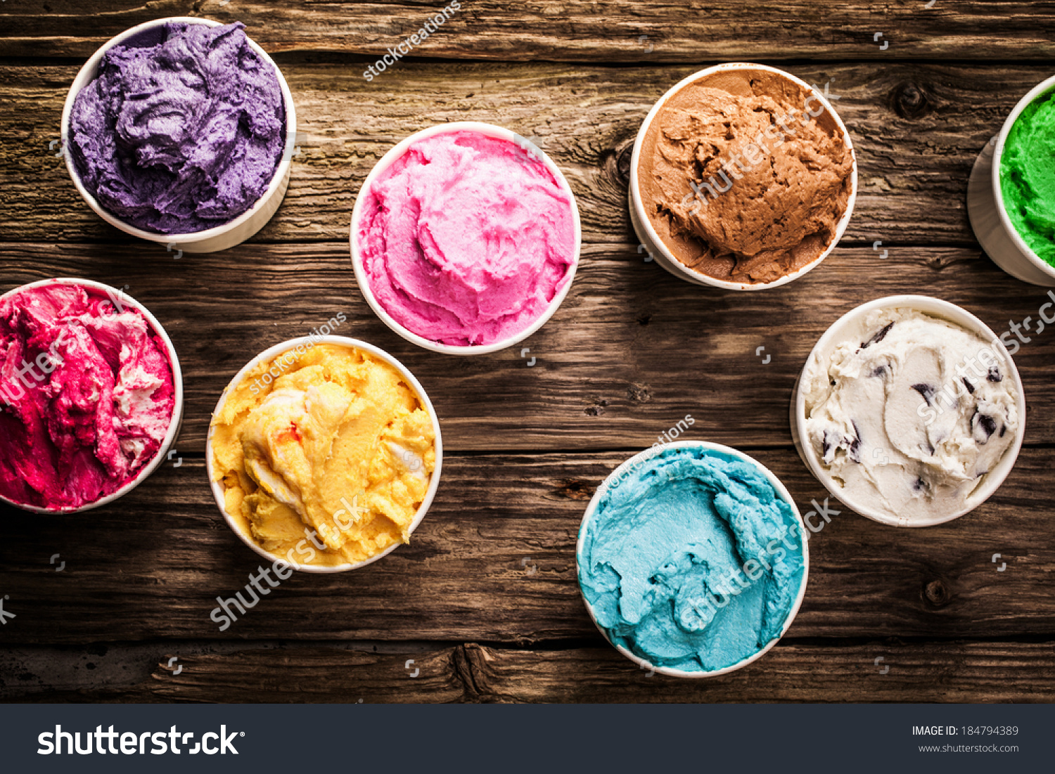 Selection of gourmet flavours of Italian ice cream in vibrant colors served in individual plastic tubs on an old rustic wooden table in an ice cream parlor, overhead view #184794389