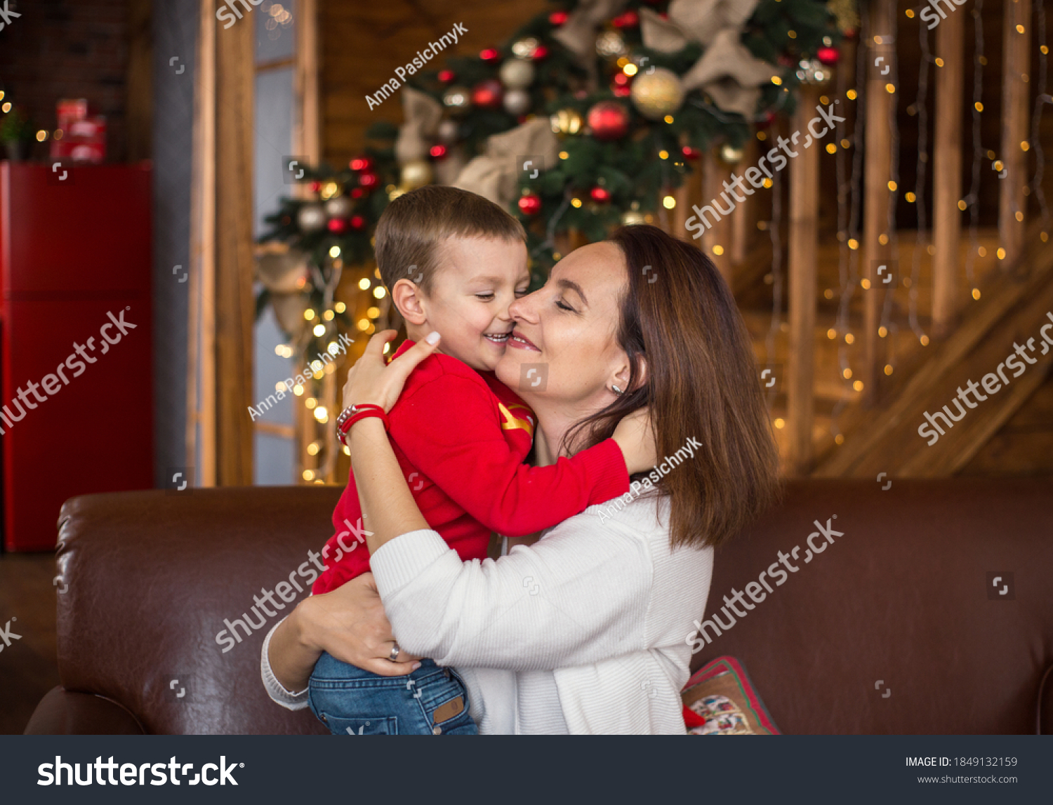 Cheerful happy mom and little son 4 years old on background of wooden house beautifully decorated before Christmas hug each other.  Cozy Christmas atmosphere #1849132159