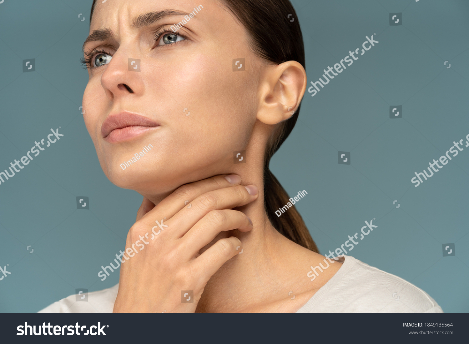 Closeup of sick woman having sore throat, tonsillitis, feeling sick, caught cold, suffering from painful swallowing, strong pain in throat, holding hand on her neck, isolated on studio blue background #1849135564