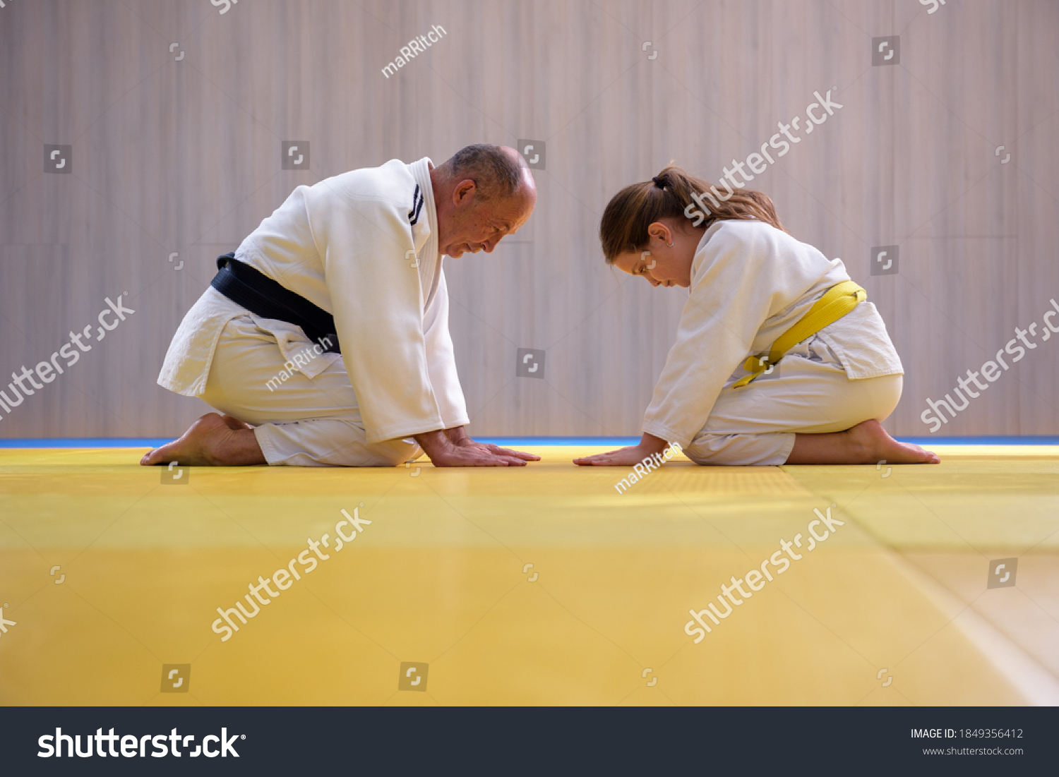 Old Judo master and young female student kneeling and bowing to each other #1849356412