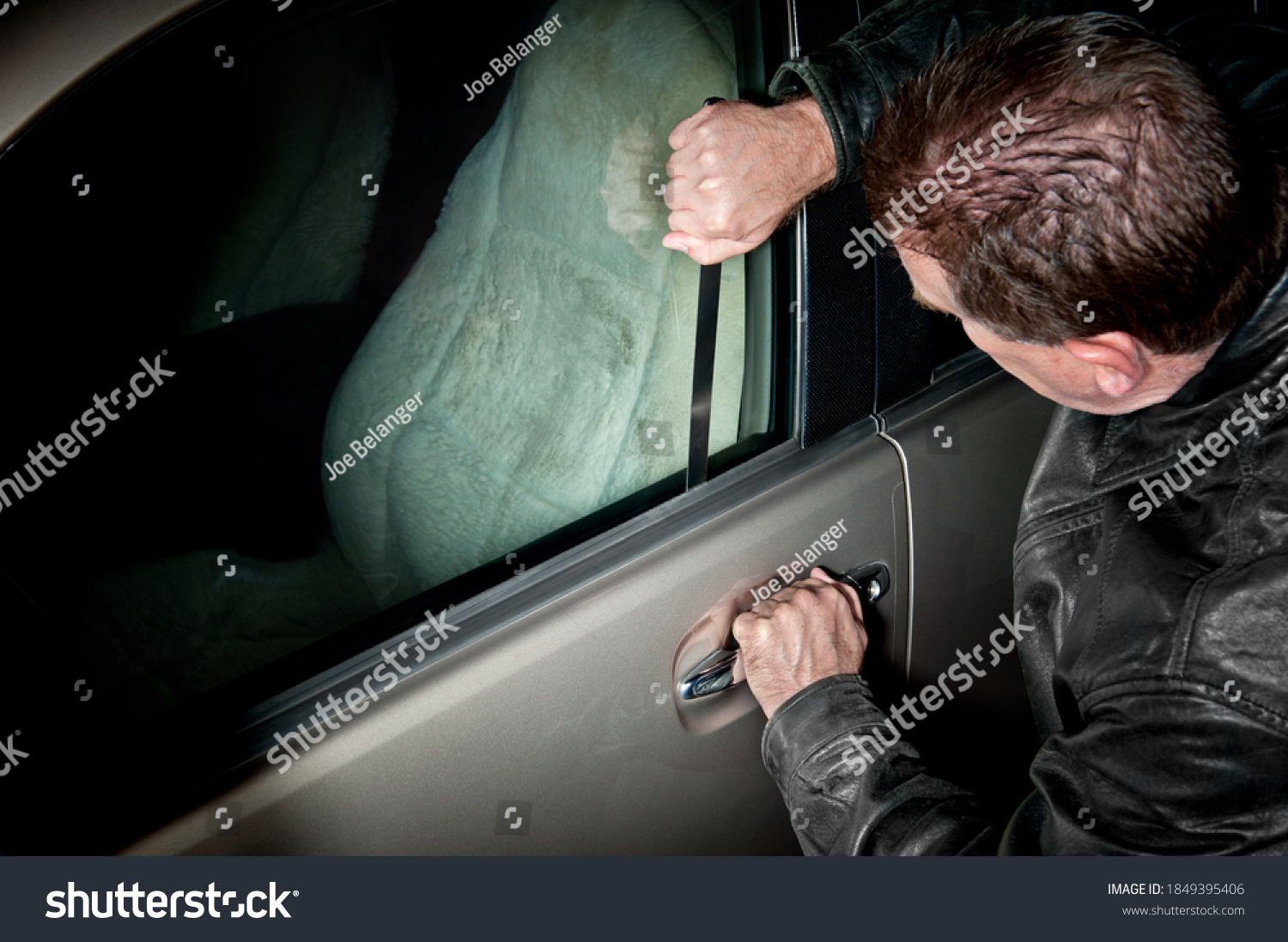 A male car thief uses a flat metal lock pick to break into a vehicle. #1849395406