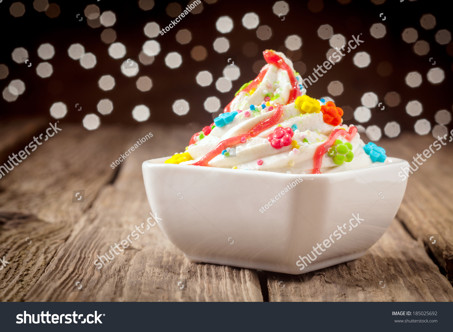 Colorful kids ice cream party dessert with a twirl of rich creamy vanilla ice cream topped with vibrant candy and sprinkles decorated with orange syrup with a bokeh of sparkling festive lights #185025692