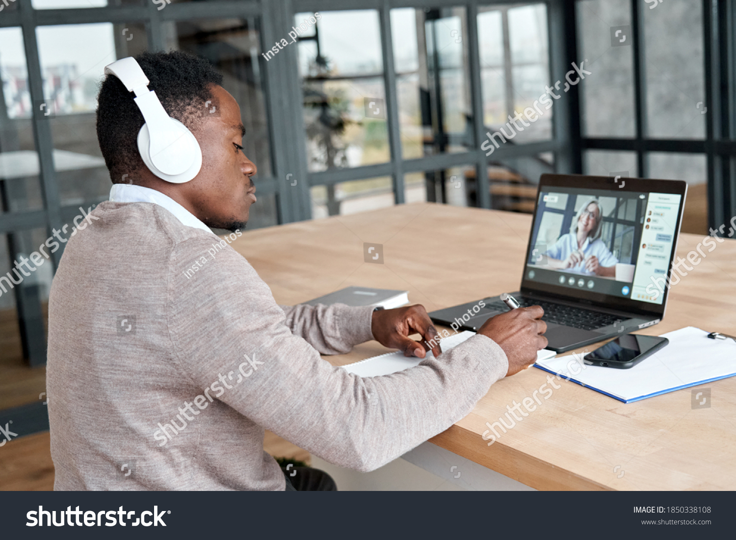 Serious african business man or black male student wearing headphones conference video calling, watching webinar online, social distance learning or working using laptop at home office, taking notes. #1850338108