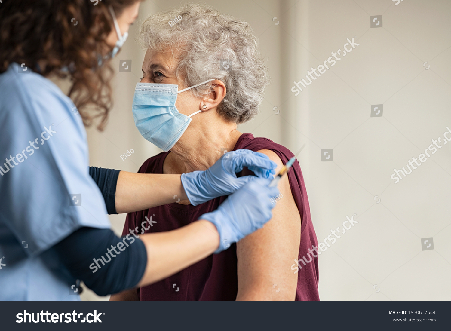 General practitioner vaccinating old patient in clinic with copy space. Doctor giving injection to senior woman at hospital. Nurse holding syringe before make Covid-19 or coronavirus vaccine. #1850607544