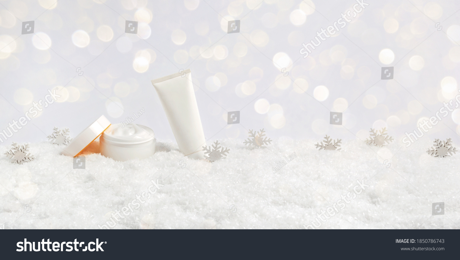 Winter skin care cosmetic products in snow and snowflakes on white background with bokeh lights. Opened face cream jar and hand creme or body lotion tube. Festive banner with copy space for text #1850786743