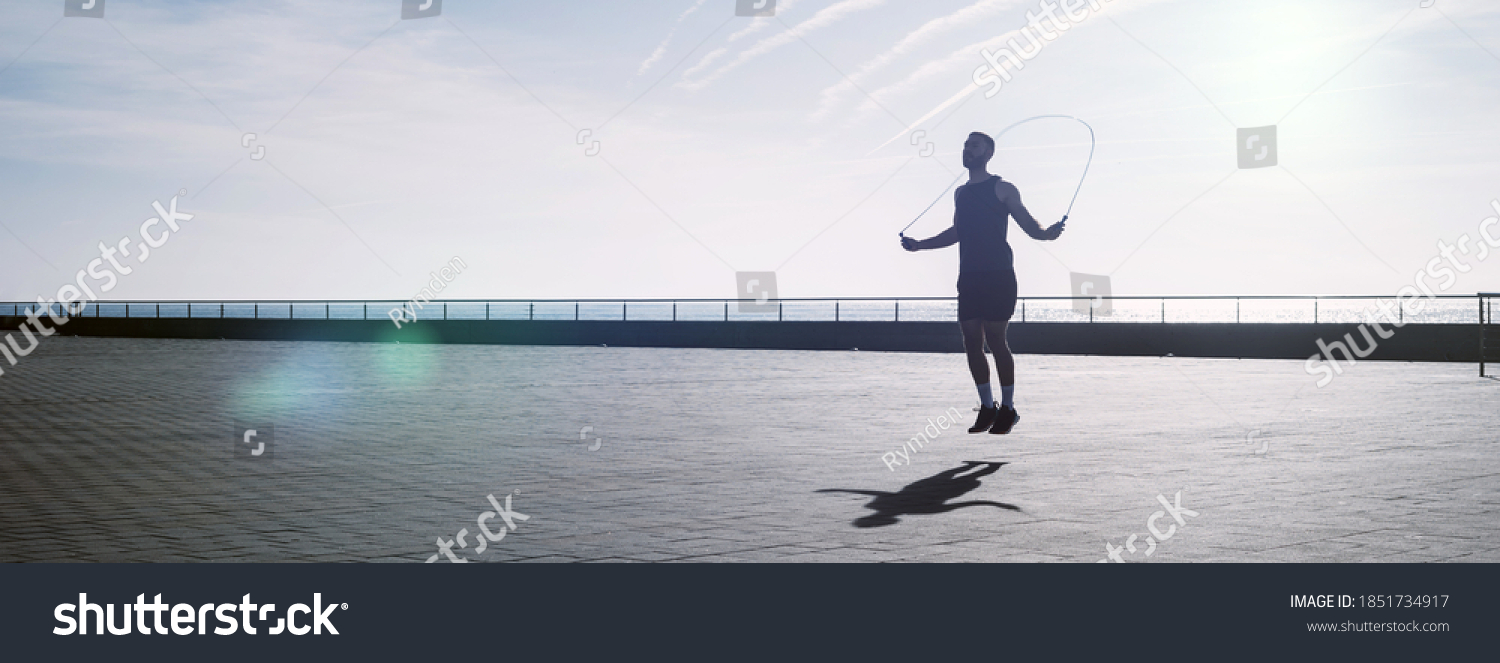 Fit young man skipping with a jump rope outdoors. Male athlete doing fitness training in morning. Workout during lockdown outside the gym. #1851734917