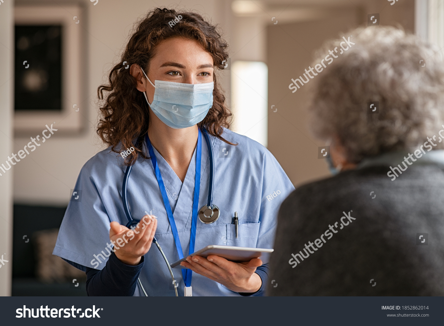 Doctor wearing safety protective mask supporting and cheering up senior patient during home visit during covid-19 pandemic. Nurse and old woman wearing facemasks during coronavirus and flu outbreak.  #1852862014