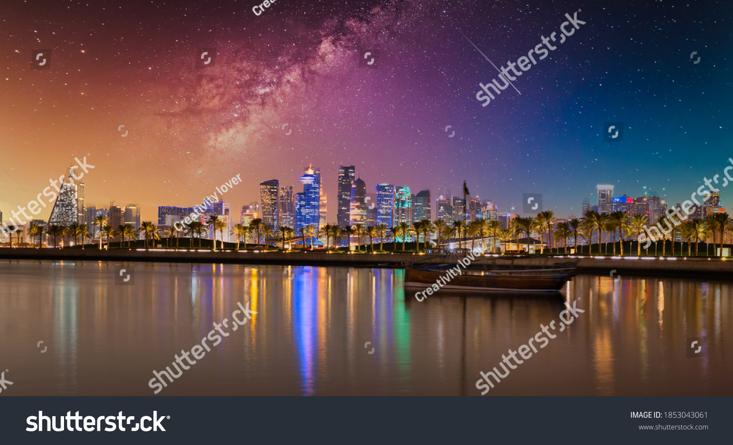 Doha Qatar skyline at night showing skyscrapers  lights reflected in the Arabic gulf and dhow in foreground with stars in sky in background #1853043061