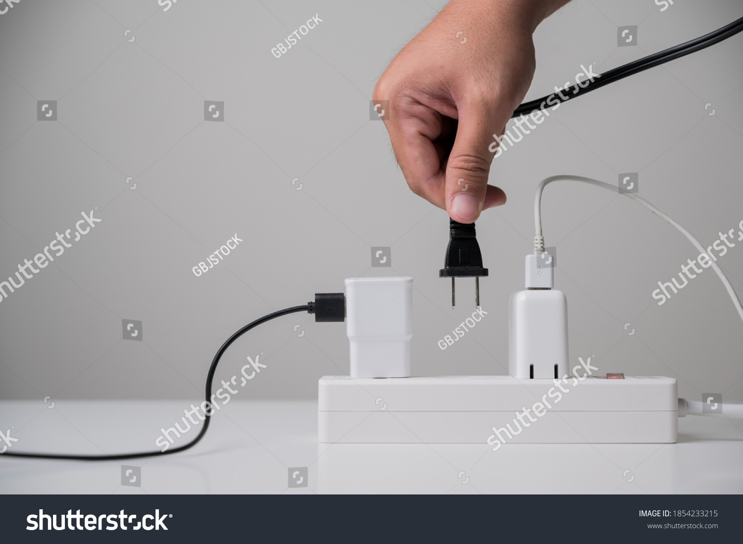 Hand holding Electric plug put on multiple socket. Electrical equipment, electrical wires and power strips in the house. Earth Hour saving electrical energy. #1854233215