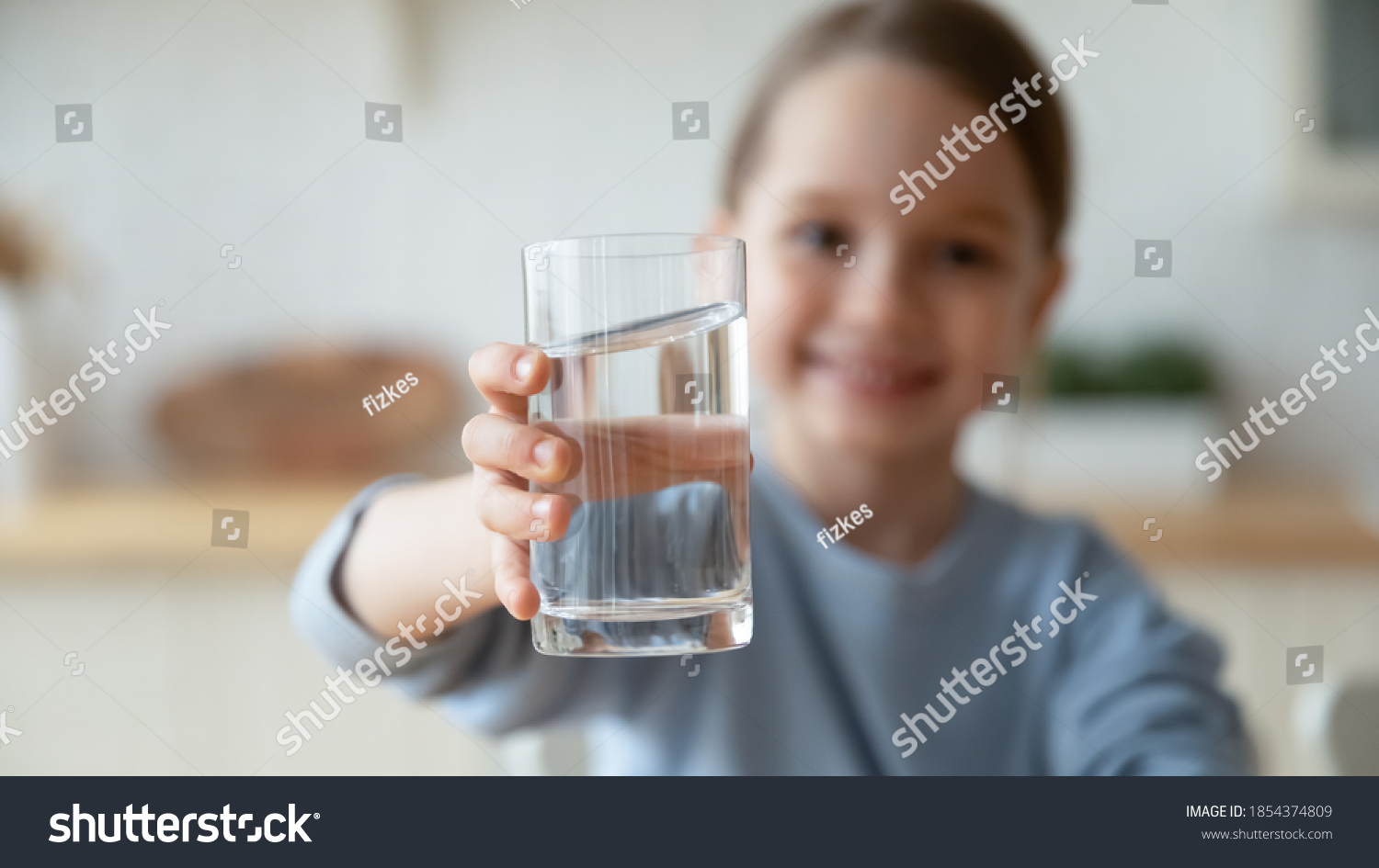 Close up smiling little girl holding glass of pure mineral water, offering to camera, cute pretty child kid recommending healthy lifestyle habit, drinking clean aqua for refreshment #1854374809
