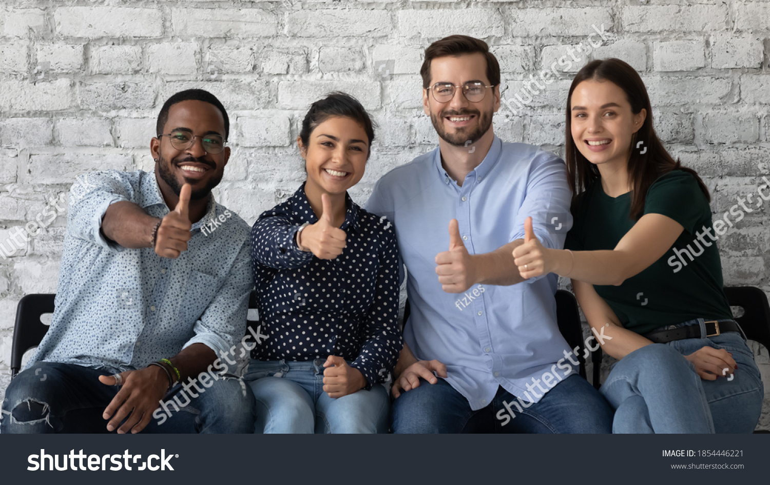 Lucky ones. Portrait of four happy satisfied multiethnic persons sitting on row of chairs in office looking at camera showing thumbs up being hired recruited getting good positions in corporate staff #1854446221