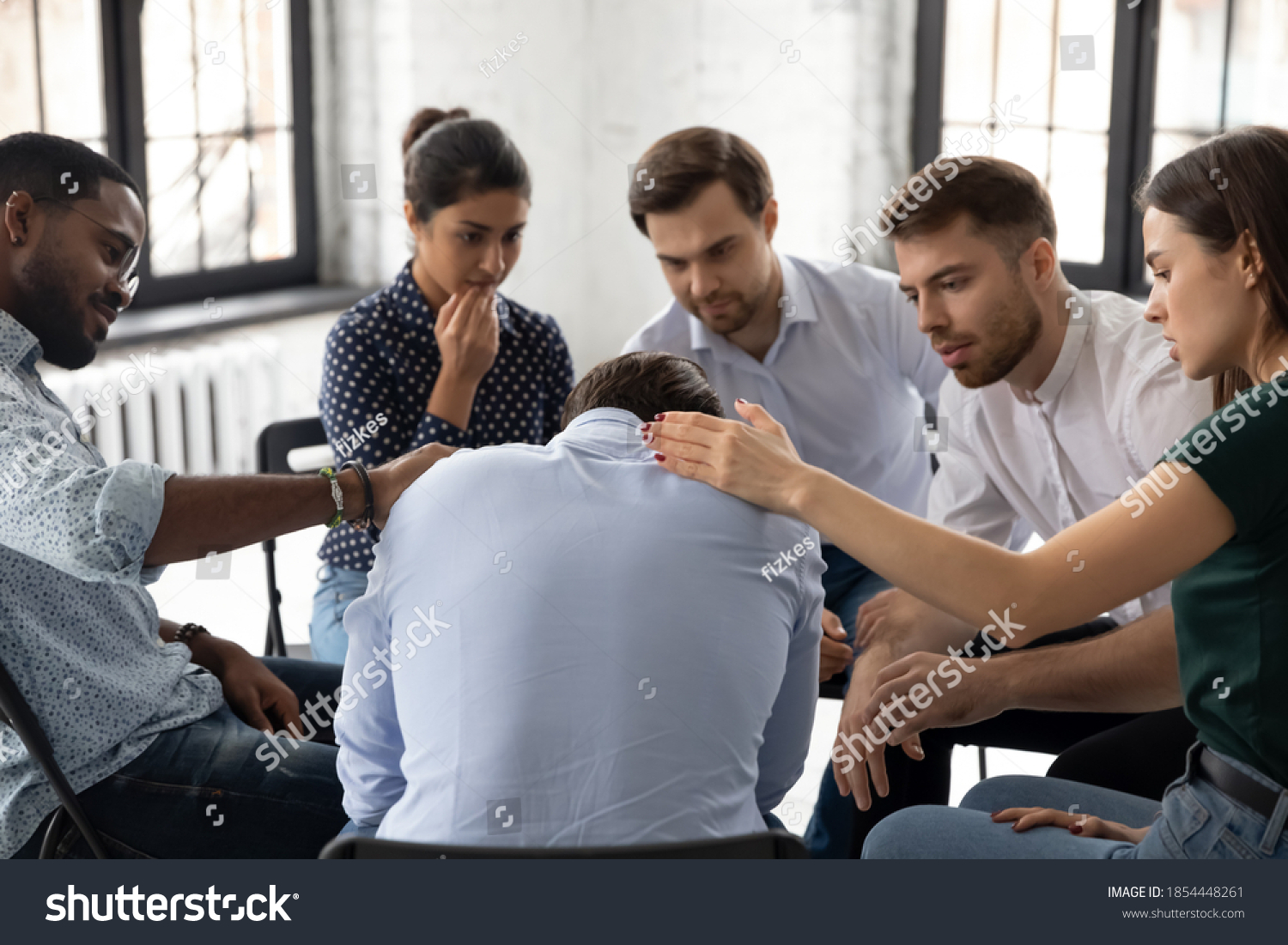 On group therapy session. Compassionate diverse multiethnic men and women gently touching shoulders of crying suffering male teammate sharing his personal problem expressing support care understanding #1854448261