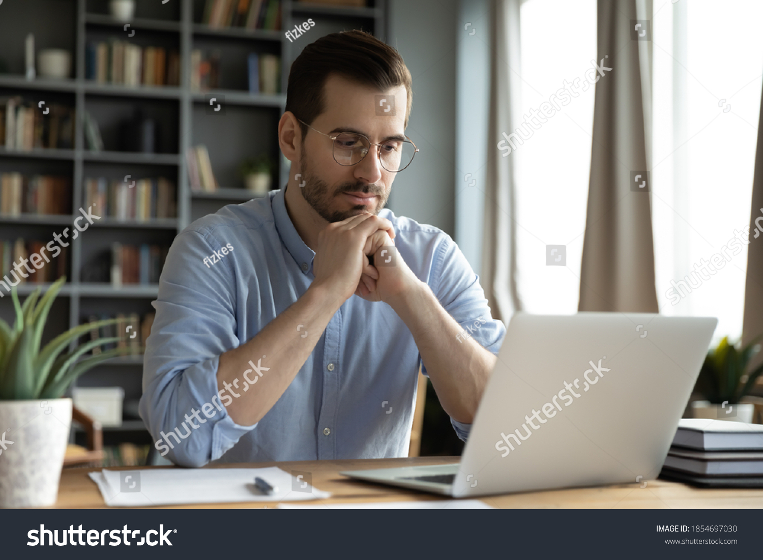 Young businessman sit at home office desk looks at laptop read media news online, learn new e app, analyzing project, stuck with challenge business task, thinks over problem, search solution concept #1854697030